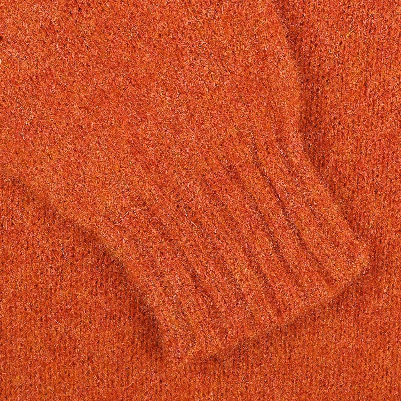 Close-up of the Orange Shetland Shaggy Dog Sweater sleeve by De Bonne Facture, featuring ribbed cuff detail and crafted from pure Shetland wool.