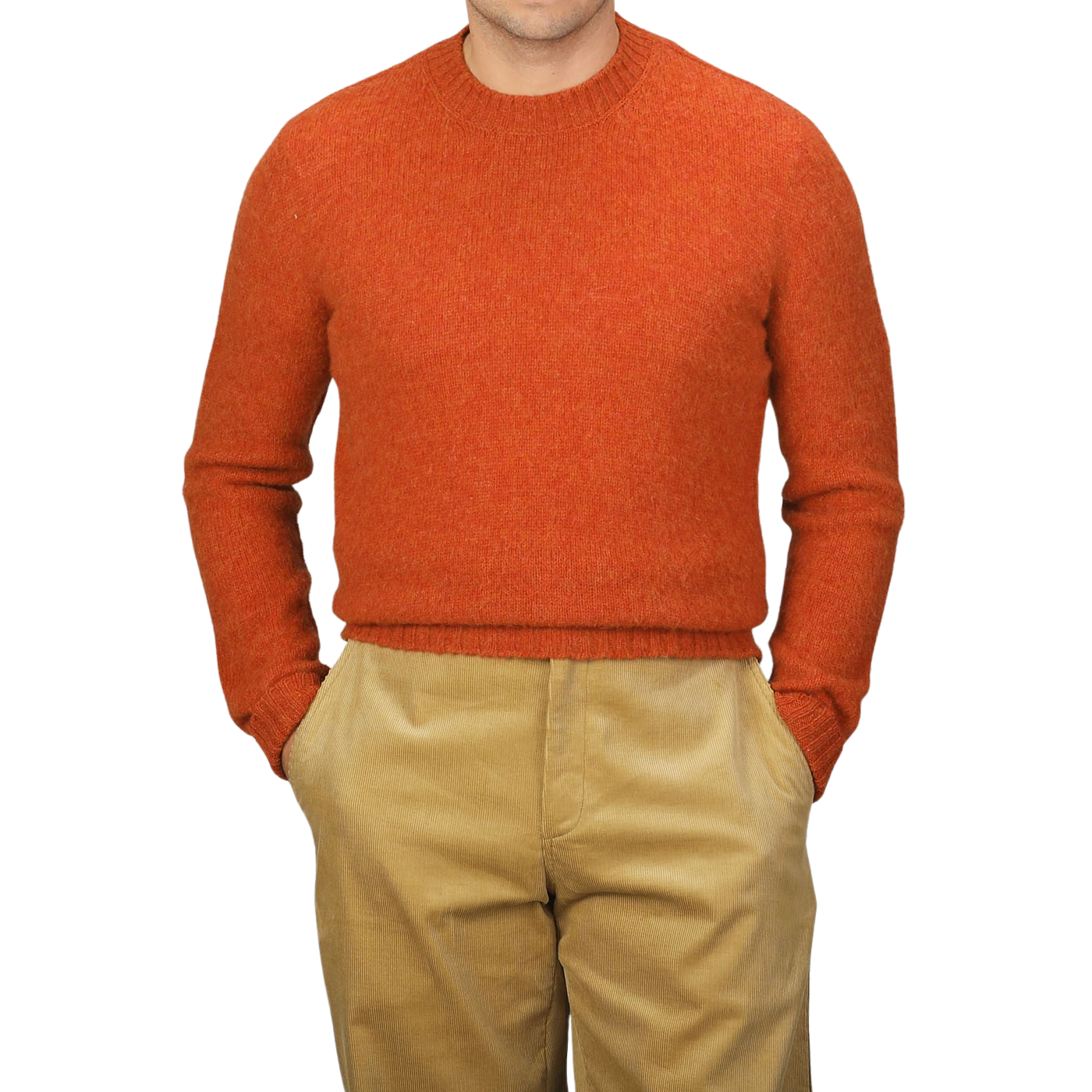 A person wearing the De Bonne Facture Orange Shetland Shaggy Dog Sweater and beige pants with hands in pockets stands against a plain background.