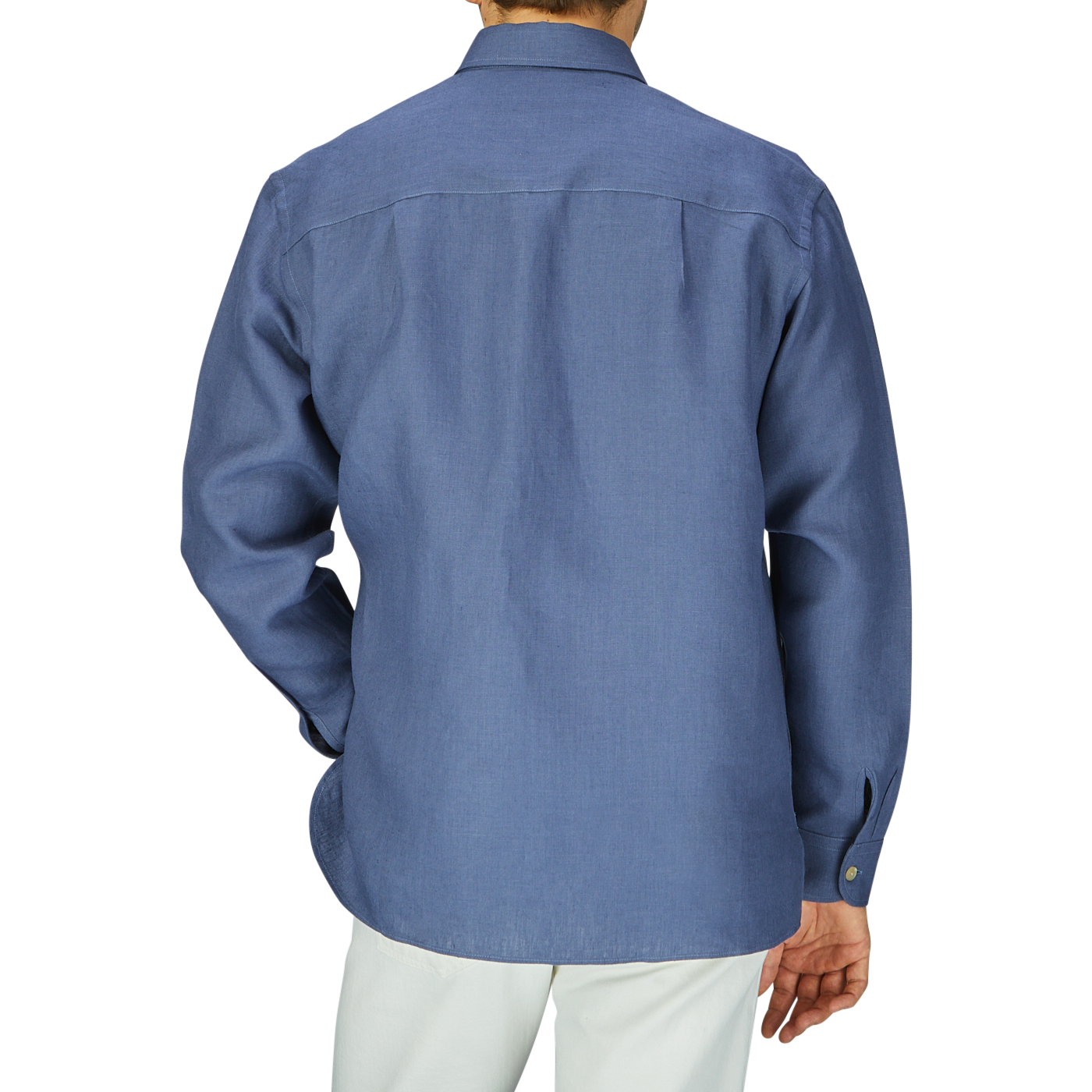 Back view of a man in a De Bonne Facture Pastel Blue Belgian Linen Two Pocket Overshirt and white pants against a grey background.