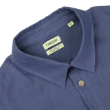 Close-up view of a Pastel Blue Belgian Linen Two Pocket Overshirt's collar and button, with a focus on the brand label reading "De Bonne Facture" inside the collar.