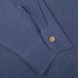 Close-up of a Pastel Blue Belgian Linen Two Pocket Overshirt cuff with a single beige button, showcasing detailed stitching on a textured fabric by De Bonne Facture.