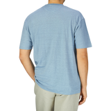Man standing with his back facing the camera, wearing a De Bonne Facture Smoke Blue Linen Jersey Oversized T-shirt and beige pants against a grey background.