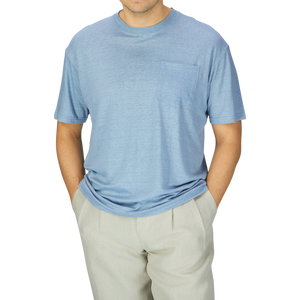 A man in a De Bonne Facture Smoke Blue Linen Jersey Oversized T-shirt and beige pants, from the chest down to the thighs, against a gray background.