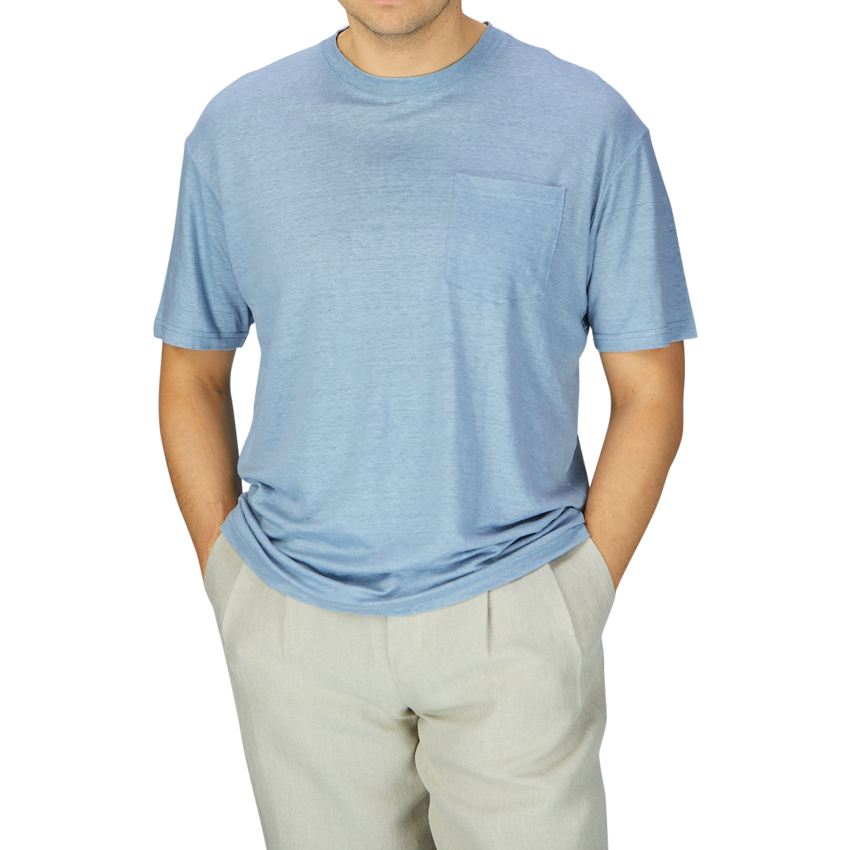 A man in a De Bonne Facture Smoke Blue Linen Jersey Oversized T-shirt and beige pants, from the chest down to the thighs, against a gray background.