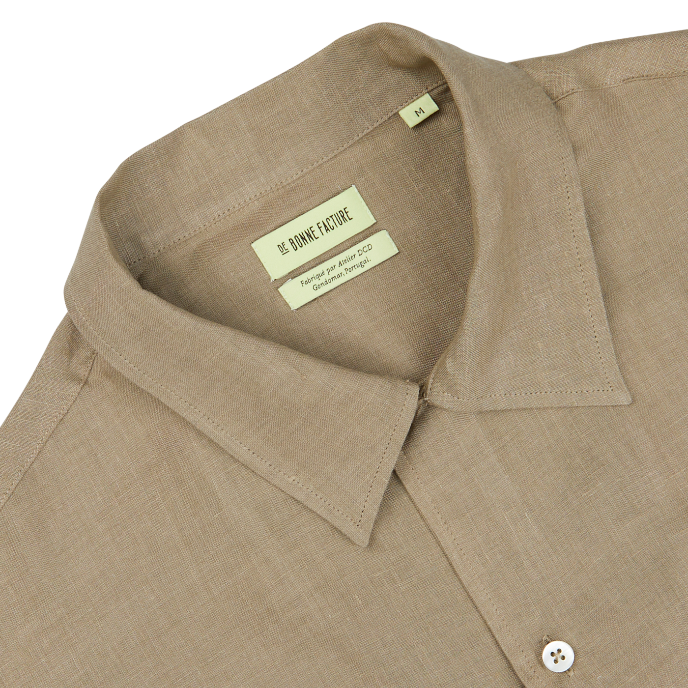 Close-up of a beige De Bonne Facture linen shirt collar with a label marking "Soft Grey Linen Floral Embroidered Shirt" and size information.