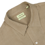 Close-up of a beige De Bonne Facture linen shirt collar with a label marking "Soft Grey Linen Floral Embroidered Shirt" and size information.
