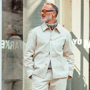 A man in a De Bonne Facture Undyed Heavy Cotton Maquignon Jacket standing outside a store.