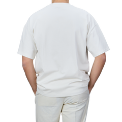 A person wearing an oversized Undyed Printed Cotton Jersey T-Shirt by De Bonne Facture and pants is shown from the back against a neutral background.