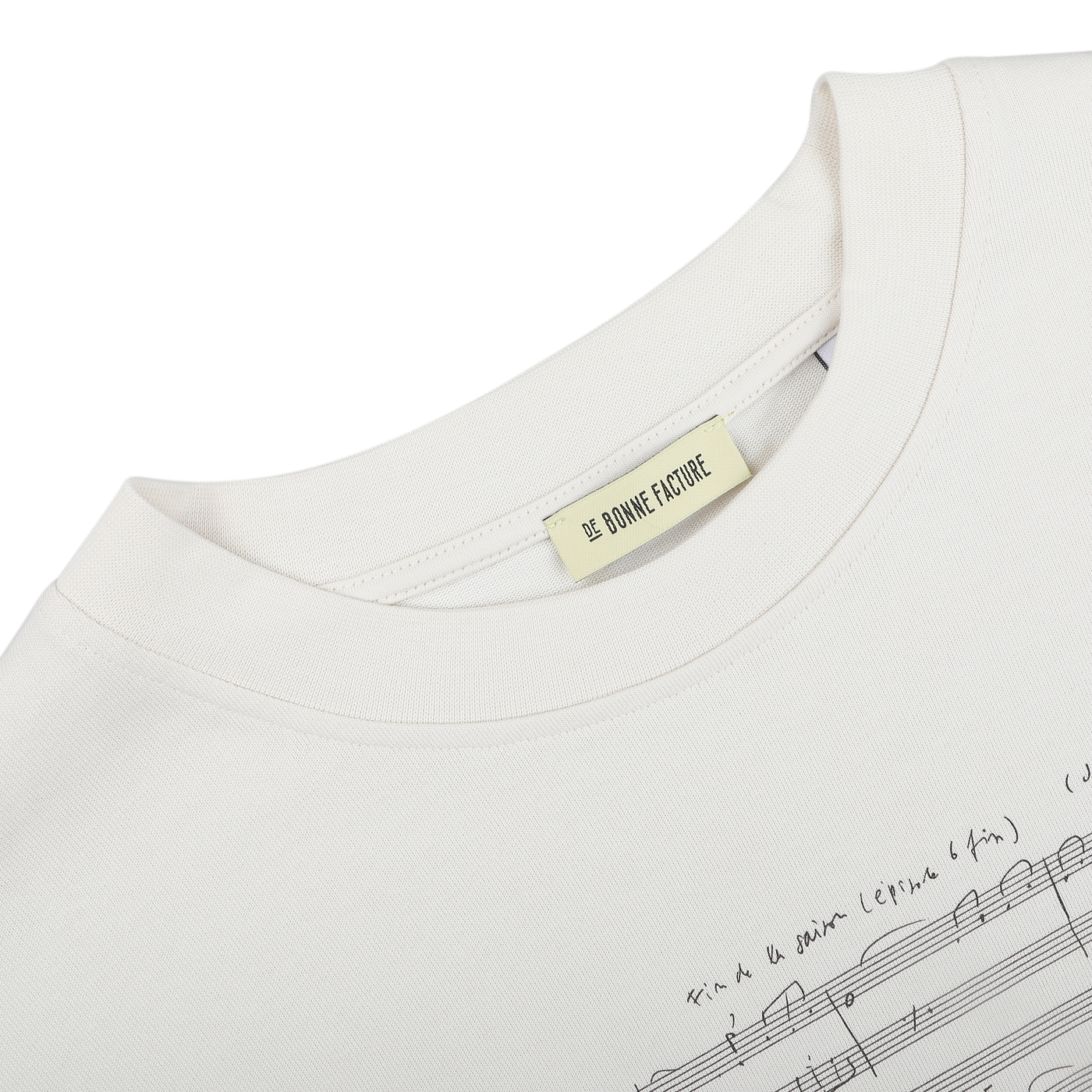 An oversized T-shirt in a natural cream hue, made from organic cotton jersey and embellished with prints of musical notes and handwriting. The label displays "De Bonne Facture.