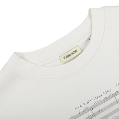 An oversized T-shirt in a natural cream hue, made from organic cotton jersey and embellished with prints of musical notes and handwriting. The label displays "De Bonne Facture.