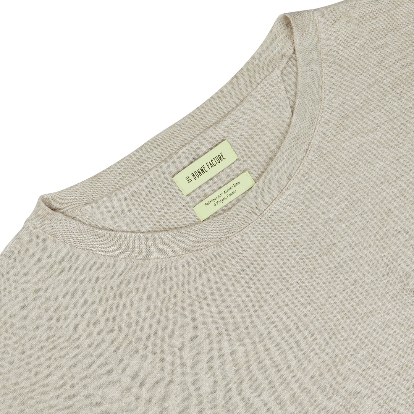Close-up of an oversized oatmeal beige linen jersey t-shirt with a label showing the brand "De Bonne Facture" and additional details, set against a white background.