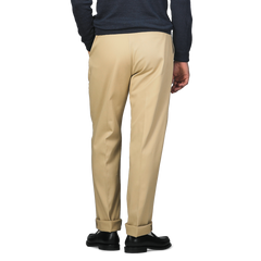 A person in a navy sweater and De Petrillo Beige Cotton Twill Modello E Trousers stands with hands in pockets, viewed from behind.