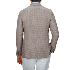 A person exudes classic elegance in the meticulously tailored De Petrillo Brown Houndstooth Wool Linen Posillipo Blazer paired with crisp white pants, viewed from the back.