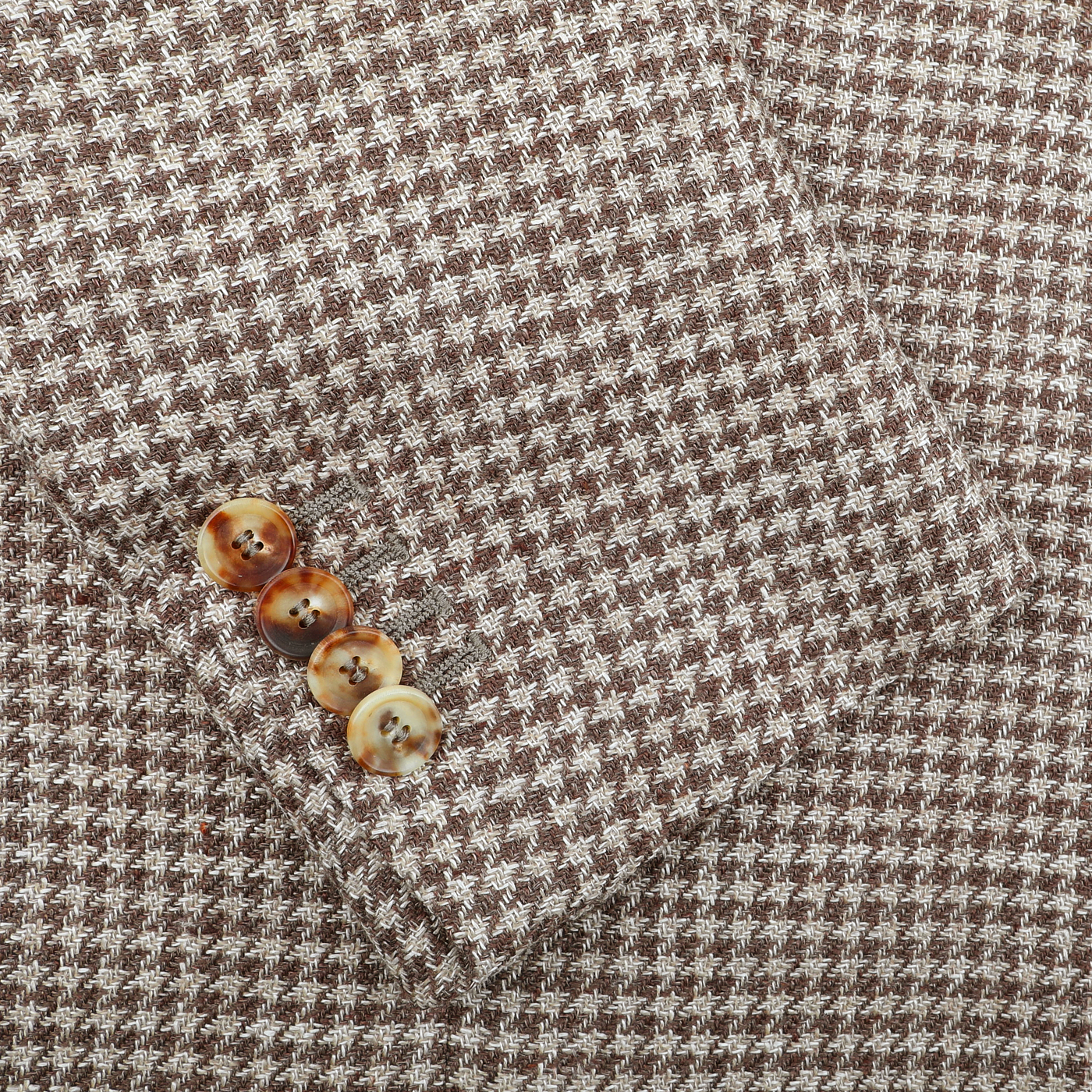 The De Petrillo Brown Houndstooth Wool Linen Posillipo Blazer is meticulously tailored with a houndstooth pattern in brown and white threads, featuring a close-up of its classic sleeve adorned with four matching brown buttons.