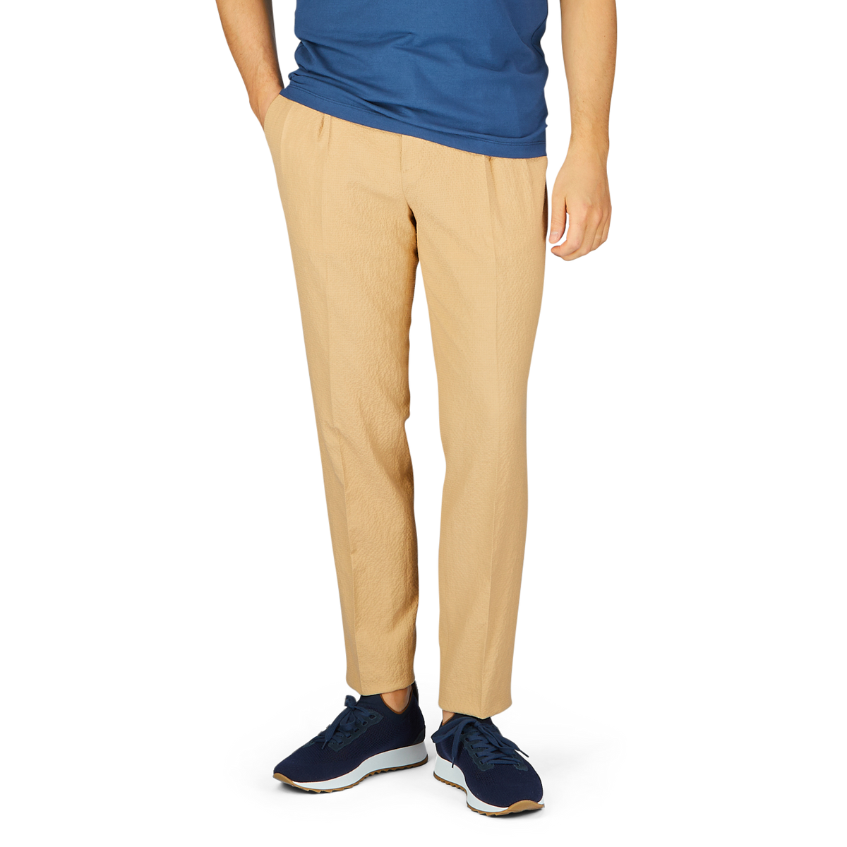 A person wearing a blue t-shirt, De Petrillo caramel cotton linen seersucker drawstring trousers, and blue sneakers, cropped at the waist.