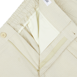 Close-up of a cream cotton seersucker drawstring De Petrillo trousers with a zipper and button closure.