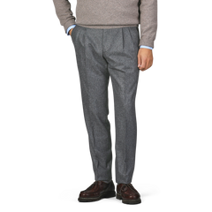 A person dressed in a gray sweater, De Petrillo's Medium Grey Wool Flannel Modello B Trousers, and dark brown shoes stands with their hands in their pockets.