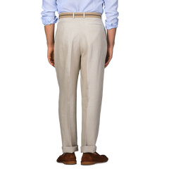 A person stands facing away wearing De Petrillo's Sand Beige Irish Linen Modello E Trousers, a light blue shirt, and brown shoes.