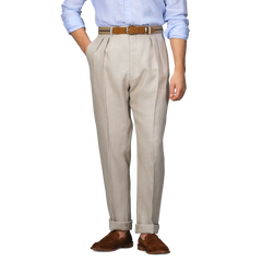 A person wearing De Petrillo Sand Beige Irish Linen Modello E Trousers, a brown belt, a light blue shirt, and brown loafers stands confidently with hands in pockets, exuding casual elegance.