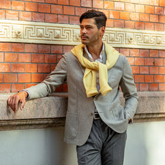 A man leaning against a brick wall wearing a De Petrillo Taupe Grey Herringbone Wool Posillipo Blazer.