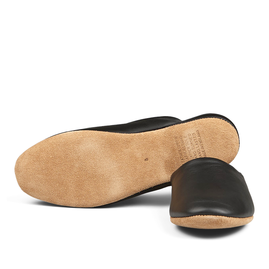 A single handmade Derek Rose black leather slipper viewed from the bottom, showing a tan sole.