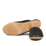 A single handmade Derek Rose black leather slipper viewed from the bottom, showing a tan sole.