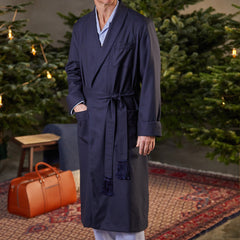 A man is standing in front of a Christmas tree wearing a Derek Rose Navy Blue Wool Twill Westminister Gown.