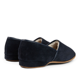 A pair of handmade navy suede sheepskin closed-back slippers by Derek Rose on a black background.