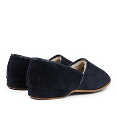 A pair of handmade navy suede sheepskin closed-back slippers by Derek Rose on a black background.