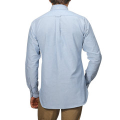 A man is seen from behind in a Blue Classic Cotton Oxford BD Shirt by Drake's, paired with beige pants against a plain background.