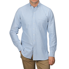 A person in a light blue Drake's Blue Classic Cotton Oxford BD Shirt, featuring a front pocket, and khaki pants stands against a plain gray background.