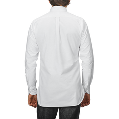 A person, viewed from behind against a gray background, wears Drake's White Classic Cotton Oxford BD Shirt with dark pants, epitomizing the classic elegance of British handmade garments.