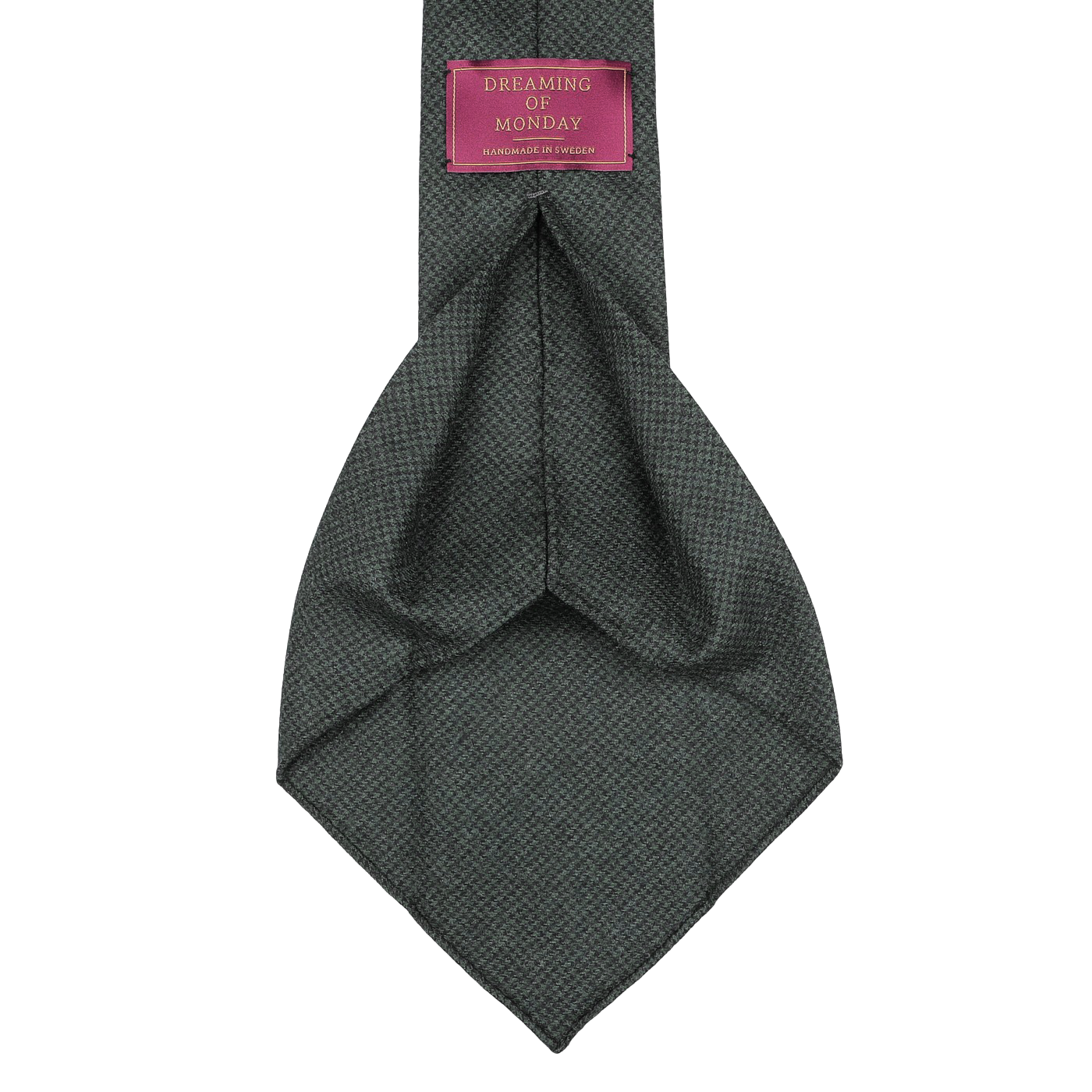 A detailed view of the Forest Green Dogtooth 7-Fold Wool Flannel Tie highlights its intricate gray pattern with a luxurious forest green texture. The tie features a pink label reading "Dreaming Of Monday," exemplifying exceptional craftsmanship in its 7-fold design. Handmade in Sweden, this Dreaming Of Monday tie embodies elegance and style.