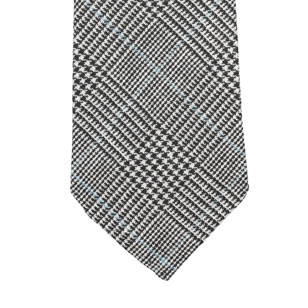 The Dreaming Of Monday Grey Prince of Wales 7-Fold Vintage Wool Tie, a plaid masterpiece in black, white, and blue, is elegantly displayed on a light gray background.