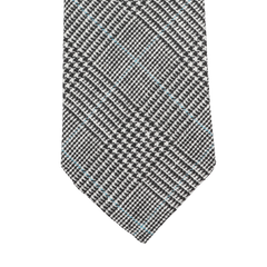 The Dreaming Of Monday Grey Prince of Wales 7-Fold Vintage Wool Tie, a plaid masterpiece in black, white, and blue, is elegantly displayed on a light gray background.