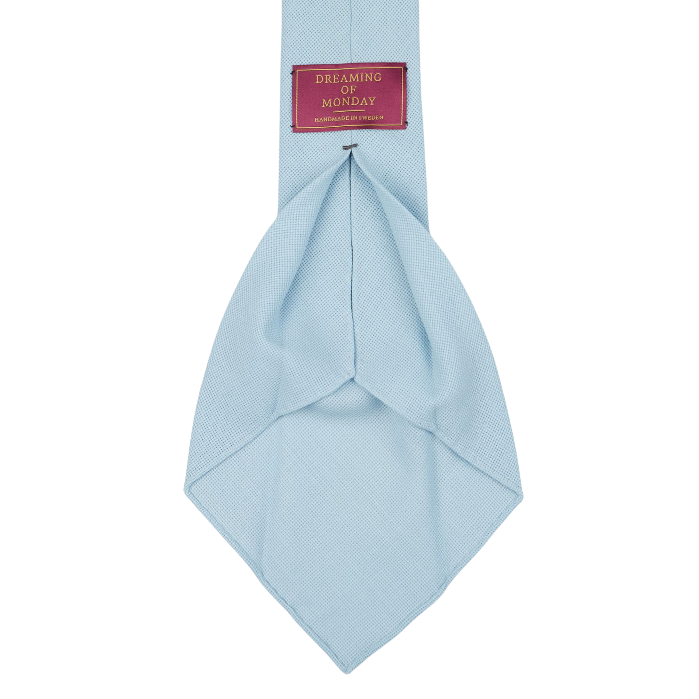 A Sky Blue 7-Fold Wool Hopsack Tie is shown, featuring a label that reads "Dreaming Of Monday" in a red rectangular box. The tie boasts an unlined 7-fold construction, ensuring both elegance and durability.