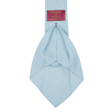 A Sky Blue 7-Fold Wool Hopsack Tie is shown, featuring a label that reads "Dreaming Of Monday" in a red rectangular box. The tie boasts an unlined 7-fold construction, ensuring both elegance and durability.