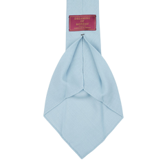 A Sky Blue 7-Fold Wool Hopsack Tie is shown, featuring a label that reads "Dreaming Of Monday" in a red rectangular box. The tie boasts an unlined 7-fold construction, ensuring both elegance and durability.