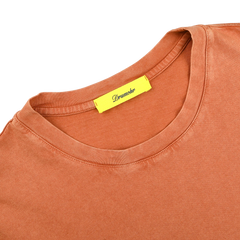 The Drumohr Burnt Orange Washed Cotton T-Shirt is a slim fit, terracotta-hued tee with a yellow "Dreamher" tag. Made in Italy, this stylish crew neck effortlessly combines comfort and elegance.