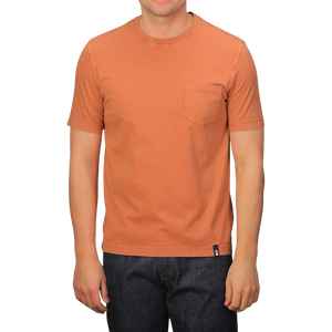 A person dons a Drumohr Burnt Orange Washed Cotton T-Shirt, featuring a slim fit and chest pocket, crafted in Italy, paired with dark jeans.