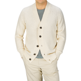 Man wearing a Ecru White Knitted Cotton Cardigan by Drumohr over a gray shirt with light-colored pants.