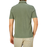 Rear view of a man wearing a Grass Green Cotton Piquet Drumohr polo shirt and beige pants against a plain background.