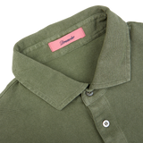 Close-up of a grass green cotton piquet polo shirt with a pink label showing the brand name "Drumohr" inside the collar.