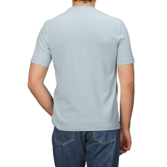 A person in a Drumohr Sky Blue Washed Cotton T-Shirt and blue jeans stands with their back to the camera, highlighting the slim fit design.