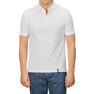 A person in a Drumohr Off-White Cotton Pique Polo Shirt and blue jeans stands against a plain background. The shirt's slim fit with a buttoned collar and small tag above the hem adds subtle detail.