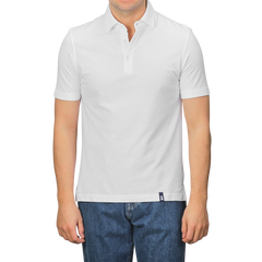 A person in a Drumohr Off-White Cotton Pique Polo Shirt and blue jeans stands against a plain background. The shirt's slim fit with a buttoned collar and small tag above the hem adds subtle detail.