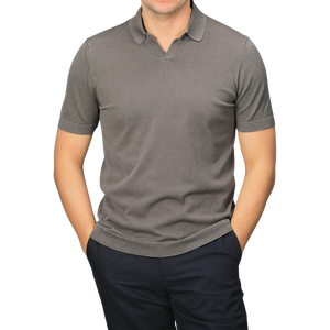 A person wearing a Drumohr Mole Washed Cotton Crepe Polo Shirt in slim fit gray with short sleeves, paired with dark pants and hands in pockets, stands against a gray background.