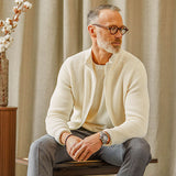 A man sitting on a chair wearing glasses and a Gran Sasso Ecru Rib Stitch Cotton Full-Zip Cardigan sweater.