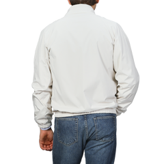 A person wearing a Fedeli Beige Nougat Nylon Reversible Blouson Jacket and blue jeans stands against a gray background, facing away from the camera.