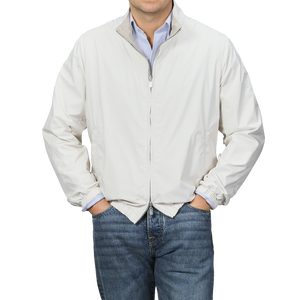 Man in a beige nougat nylon reversible Fedeli blouson jacket over a blue striped shirt with jeans, against a gray background.